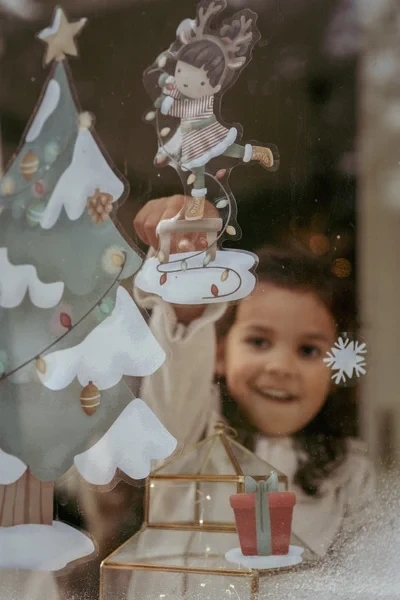 Dziecko dekoruje okno naklejkami Choinka X-MAS Little Dutch – kreatywna zabawa świąteczna