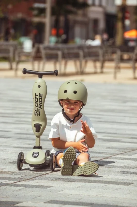 Dziecko w kasku Scoot and Ride Olive obok hulajnogi