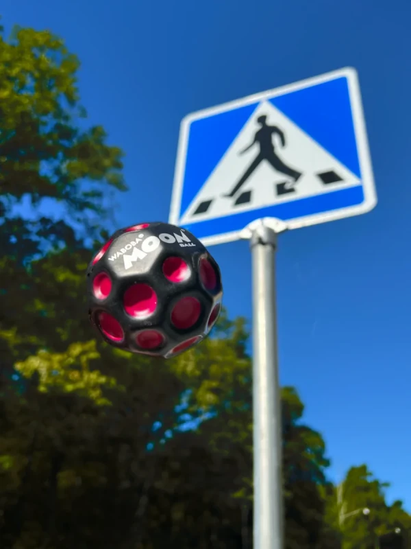 Piłeczka Waboba UV Moon Ball odbijająca się na tle znaku drogowego
