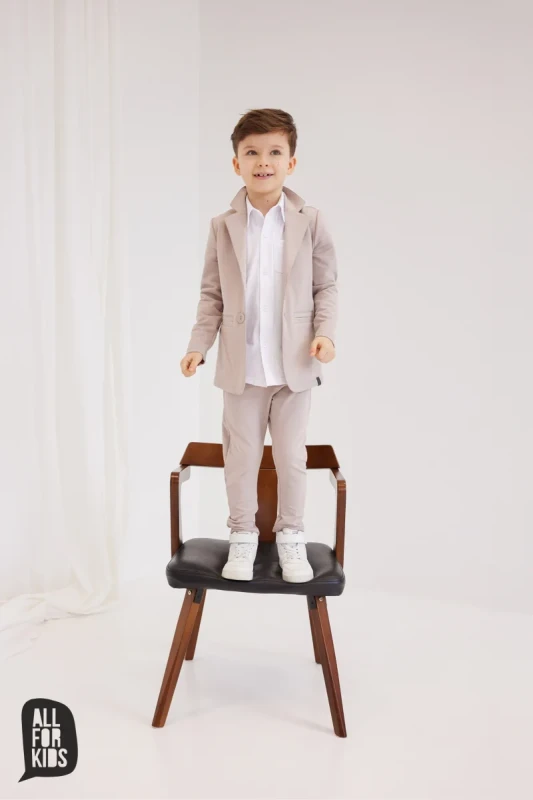 chłopiec w beżowych dzianinowych spodniach dziecięcych all for kids stojący na krześle