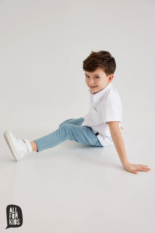 chłopiec siedzący w białej koszuli dziecięcej all for kids błękitne spodnie