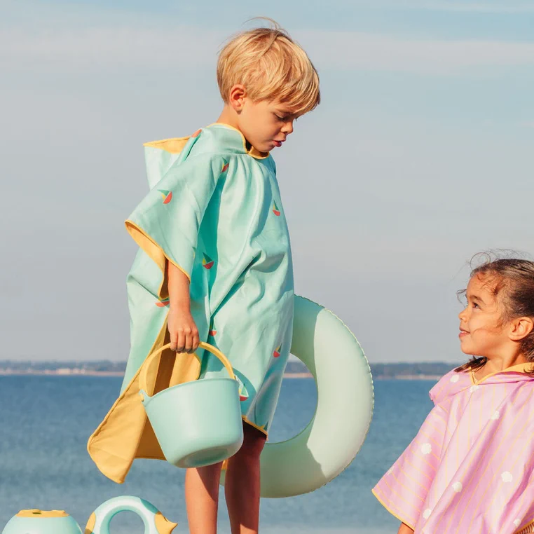 Dziecko w poncho plażowym QUUT Banana Blue nad morzem