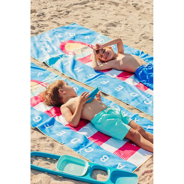 Dzieci odpoczywają na ręcznikach QUUT PlayTowels Lighthouse Blue na plaży