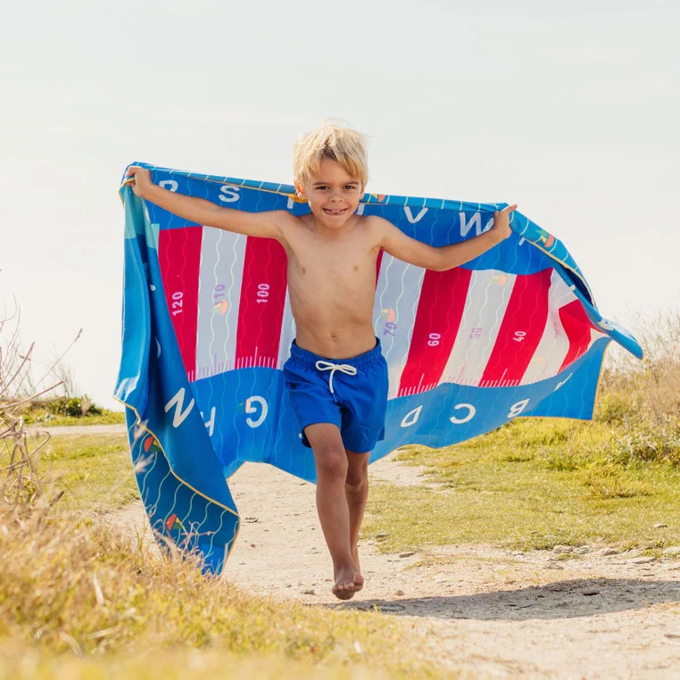 Chłopiec biegnie z ręcznikiem QUUT PlayTowels Lighthouse Blue