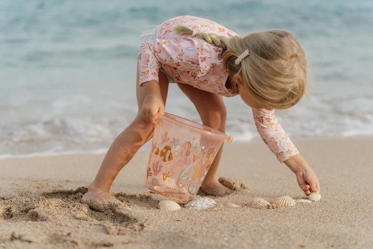 Dziecko zbierające muszelki z wiaderkiem Little Dutch Pink Ocean Dreams na plaży